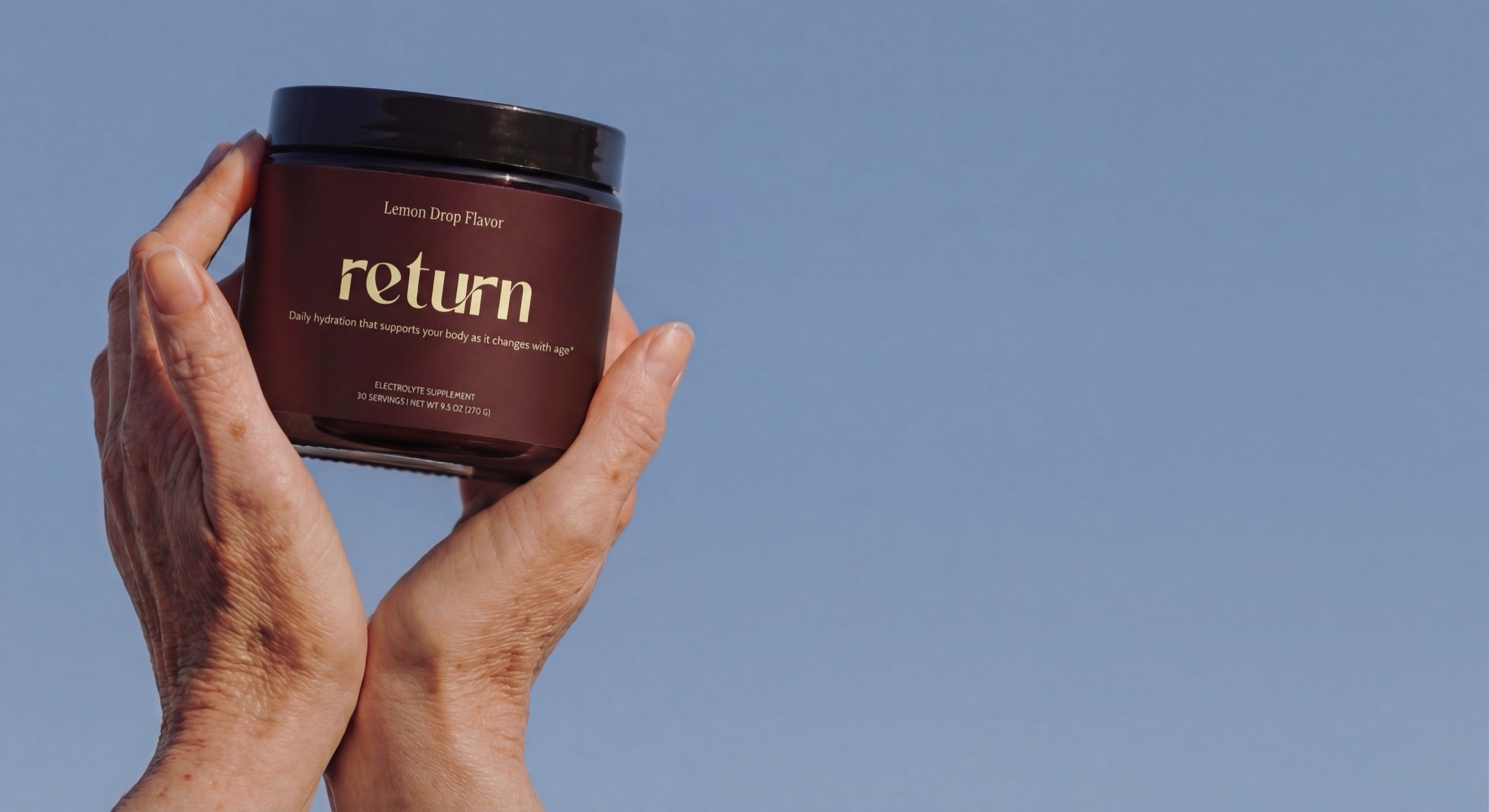 Return Hydration Lemon Drop held against a clear blue sky